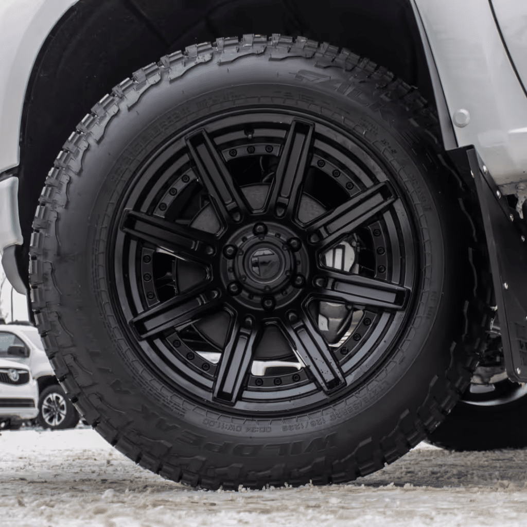 Black alloy wheel with aggressive tread tire on a white truck, showcasing attention to off-road performance and style.