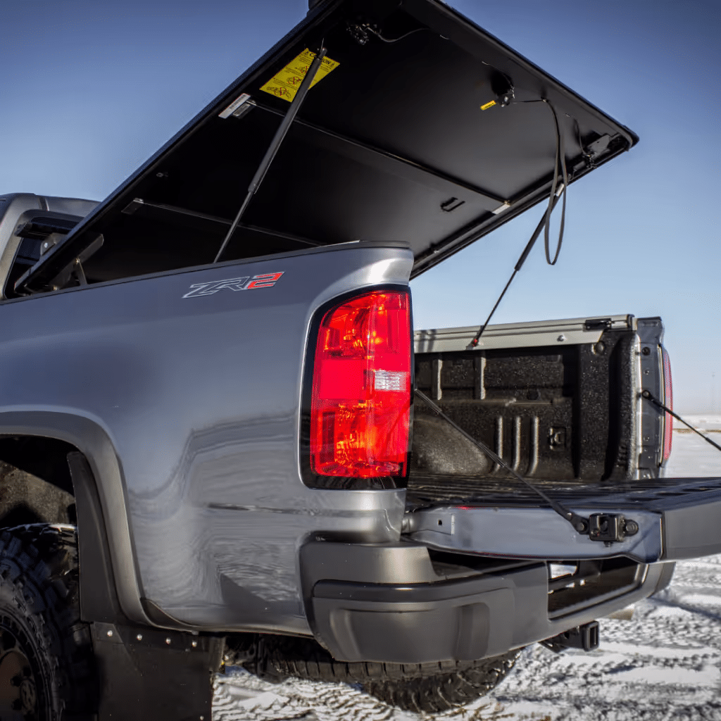 Close-up view of the open tailgate of a gray ZR2 pickup truck, showcasing the truck bed and its accessories against a snowy landscape.