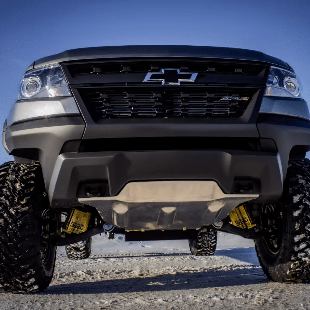 Close-up view of a lifted Chevrolet truck showcasing its rugged front grille, robust tires, and advanced suspension system, set against a clear blue sky. Ideal for off-road enthusiasts and truck lovers.