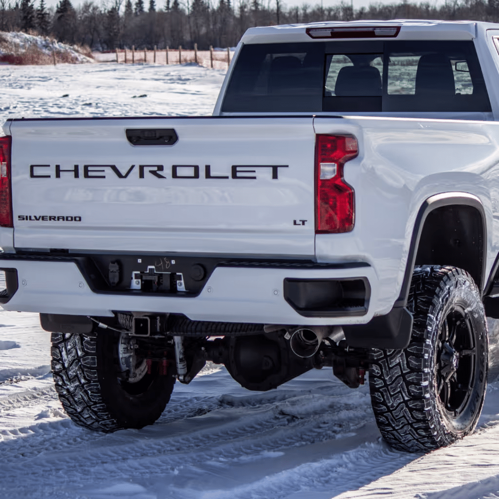 White Chevrolet Silverado LT truck parked on snowy terrain, showcasing large black wheels and rear bumper design, with clear visibility of the Chevrolet branding on the tailgate.
