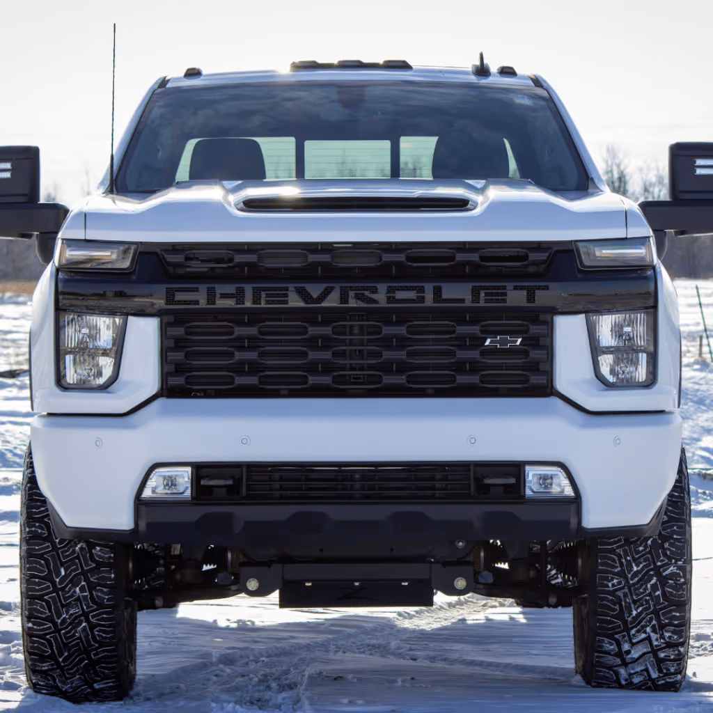 Front view of a white Chevrolet truck showcasing its bold grille and rugged design, parked on snowy terrain. Ideal for demonstrating durability and performance in various driving conditions.