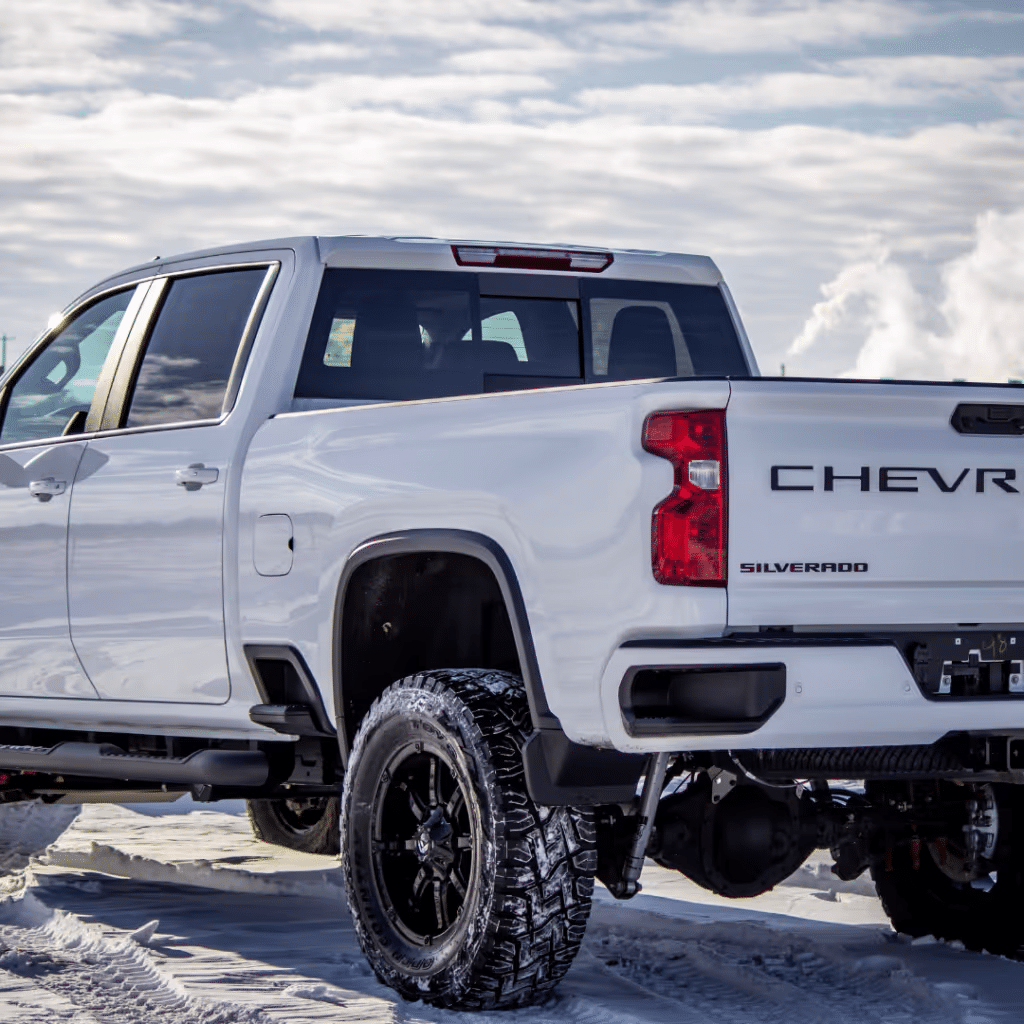 White Chevrolet Silverado pickup truck parked in snow, showcasing its rugged design and off-road tires under a cloudy sky.