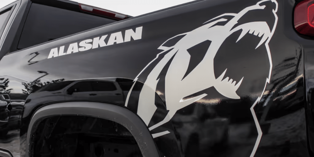 Close-up of a black truck showcasing an Alaskan-themed decal featuring a white bear graphic, emphasizing rugged outdoor aesthetics. The image highlights the truck’s rear design elements and branding.