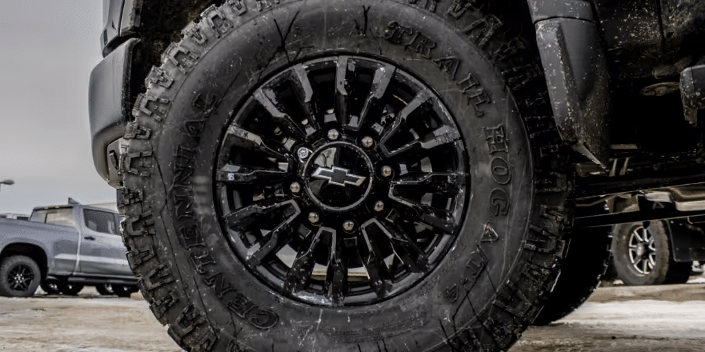 Close-up of a black Chevrolet truck wheel featuring rugged off-road tires with aggressive tread patterns, showcasing the vehicle's capability for adventurous terrains.