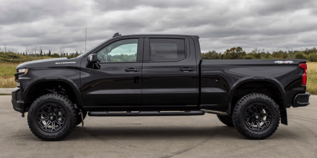 Black Chevrolet Silverado truck with off-road tires and a lifted suspension, showcasing a sleek side profile against a cloudy backdrop. Ideal for outdoor and rugged terrains.