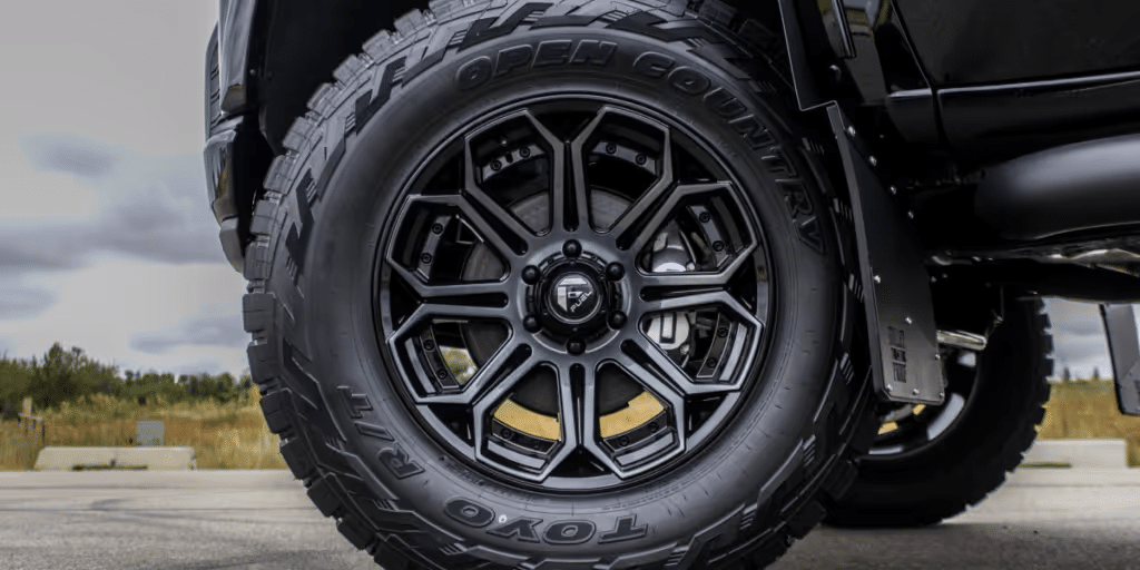 Close-up view of a premium black alloy wheel mounted on a rugged off-road tire, showcasing the TOYO Open Country tread design, ideal for durability and traction on various terrains.