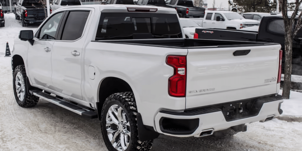 A white Chevrolet Silverado truck parked in snowy conditions, showcasing its sleek design and chrome accents, with other trucks visible in the background.