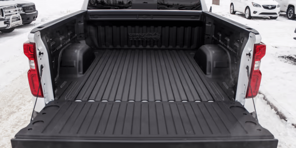 Interior view of a pickup truck bed showcasing a durable rubber liner, designed for heavy-duty use, with snow visible in the background, emphasizing outdoor functionality and versatility.