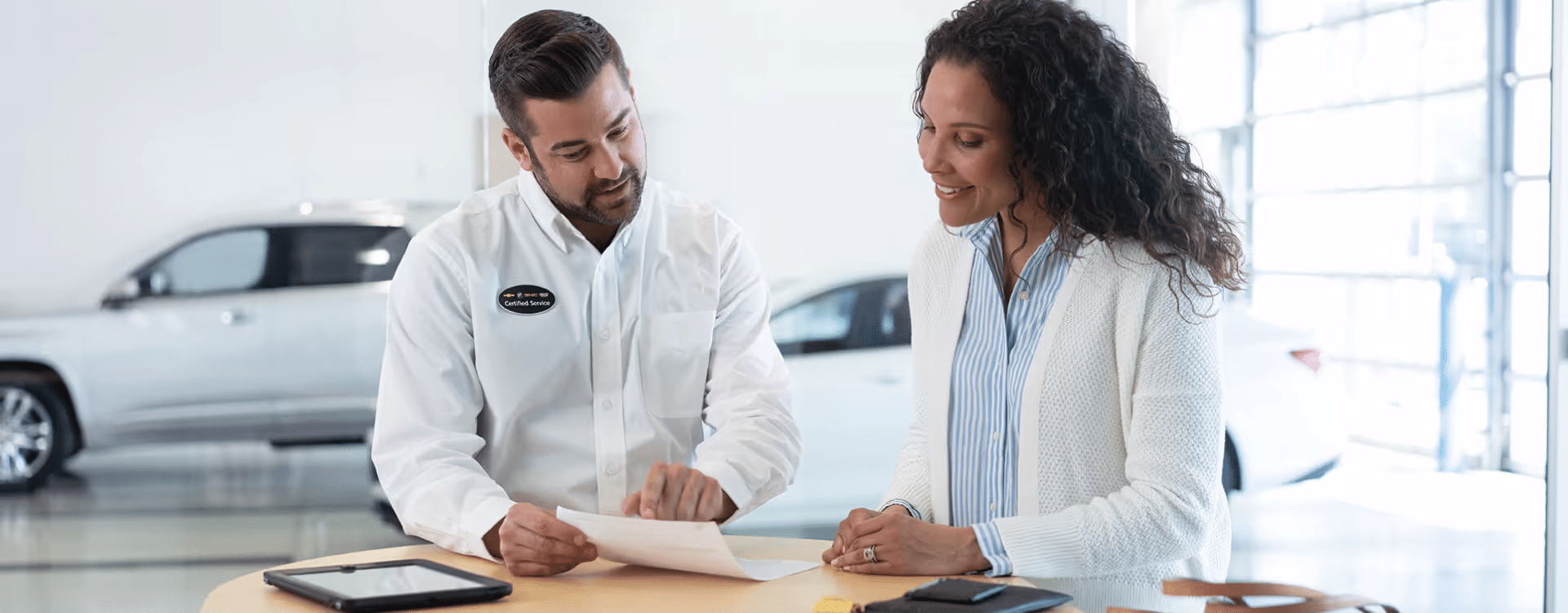 A car dealership employee reviews paperwork with a smiling female customer at a modern showroom, emphasizing personalized customer service and vehicle purchasing guidance.