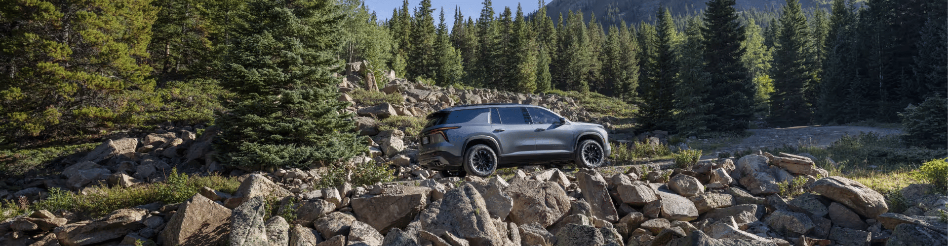A rugged SUV parked on a rocky terrain surrounded by dense pine trees and mountains, showcasing its off-road capability in a natural landscape.