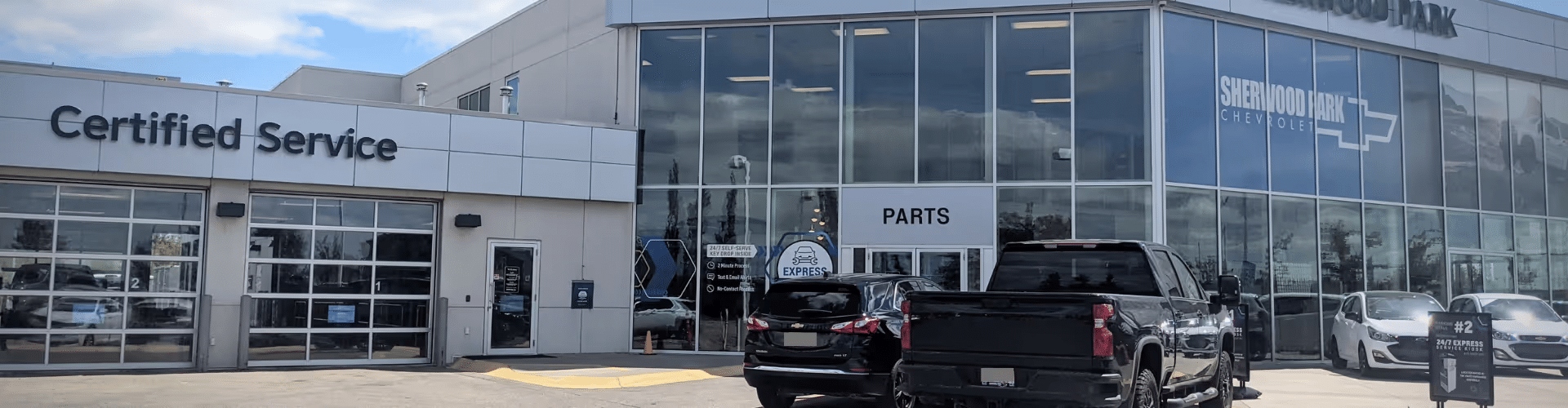 Exterior view of Sherwood Park Chevrolet dealership showcasing the Certified Service and Parts department, with several vehicles parked outside, under clear blue skies.