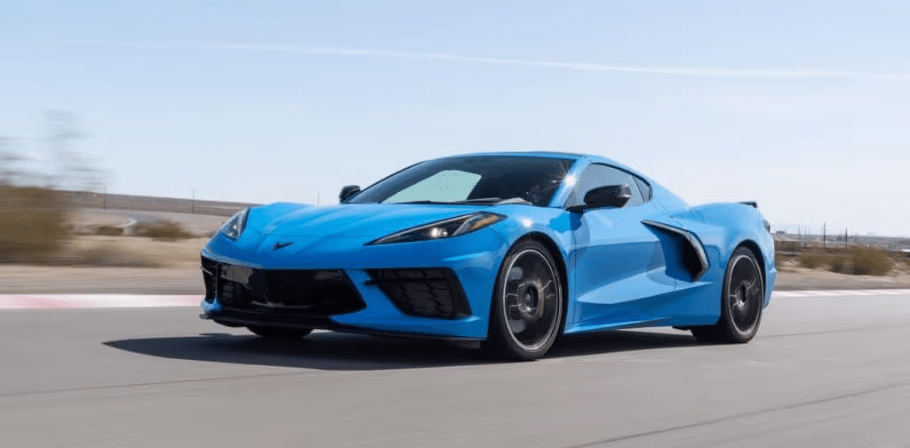 Blue Chevrolet Corvette C8 speeding on a race track under clear skies, showcasing its sleek design and performance capabilities.
