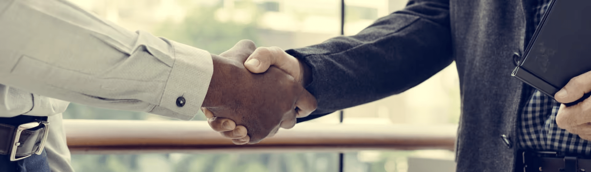 Close-up of two individuals shaking hands in a professional setting, symbolizing partnership and collaboration, with a blurred cityscape backdrop.
