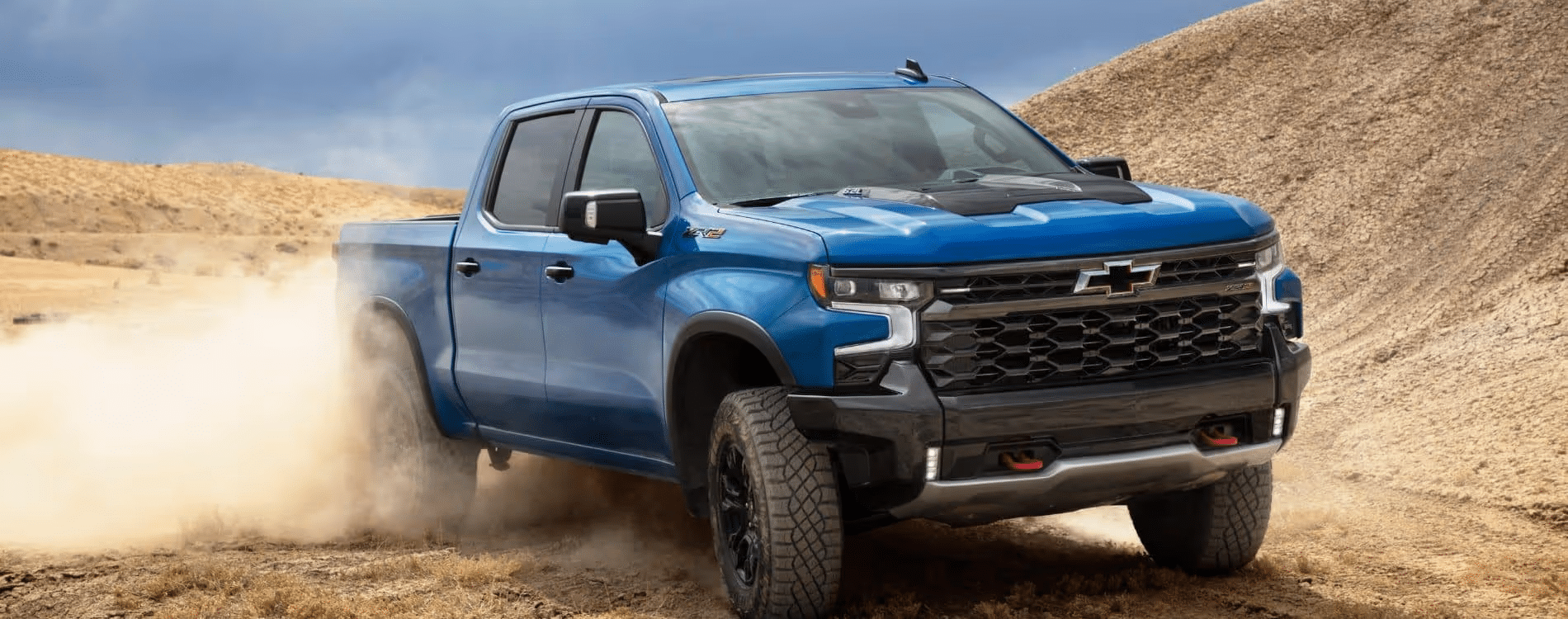 Powerful blue Chevrolet Silverado truck driving through sandy terrain, showcasing its off-road capabilities and rugged design.
