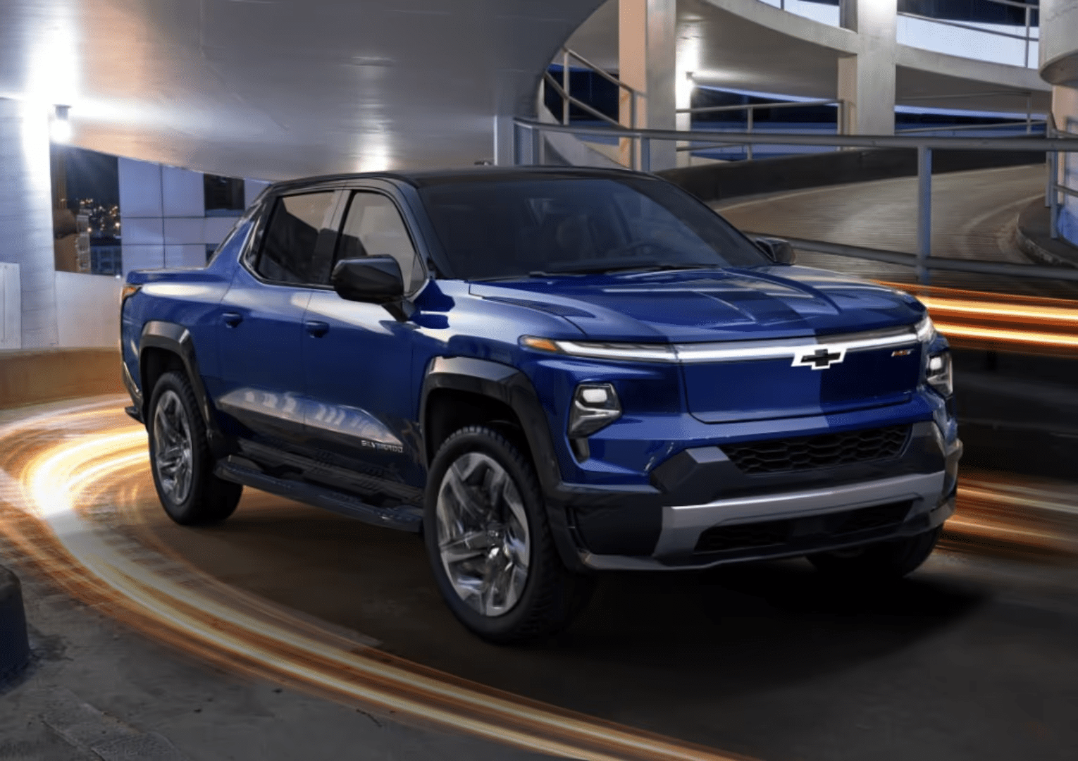 A sleek grey Chevrolet SUV parked in front of a modern architectural building with large glass windows and textured stone walls, showcasing contemporary design and automotive innovation.