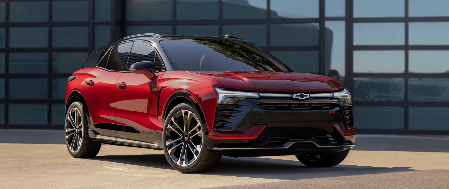 A sleek red Chevrolet SUV parked in front of modern glass architecture, highlighting its bold design features, including angular headlights and stylish alloy wheels, representing a blend of performance and elegance.