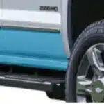 Close-up of a truck's side, featuring custom blue trim and a chrome wheel. The image highlights the truck's rugged design and sturdy running board, showcasing its off-road capabilities.