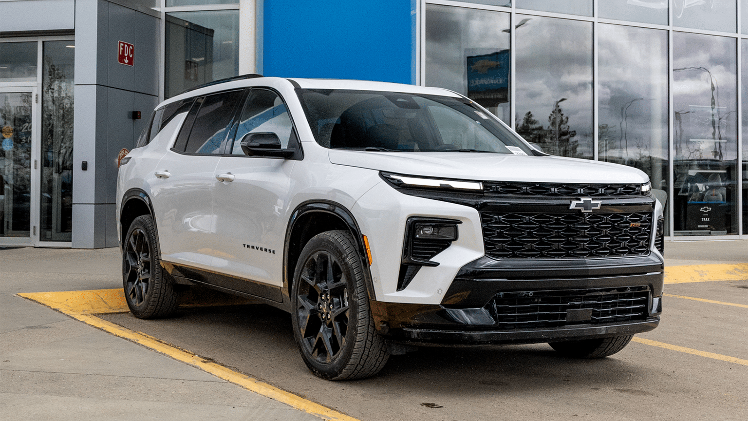 White Chevrolet Traverse RS parked outside a dealership, showcasing its sleek design and modern features, including a prominent front grille and stylish alloy wheels.
