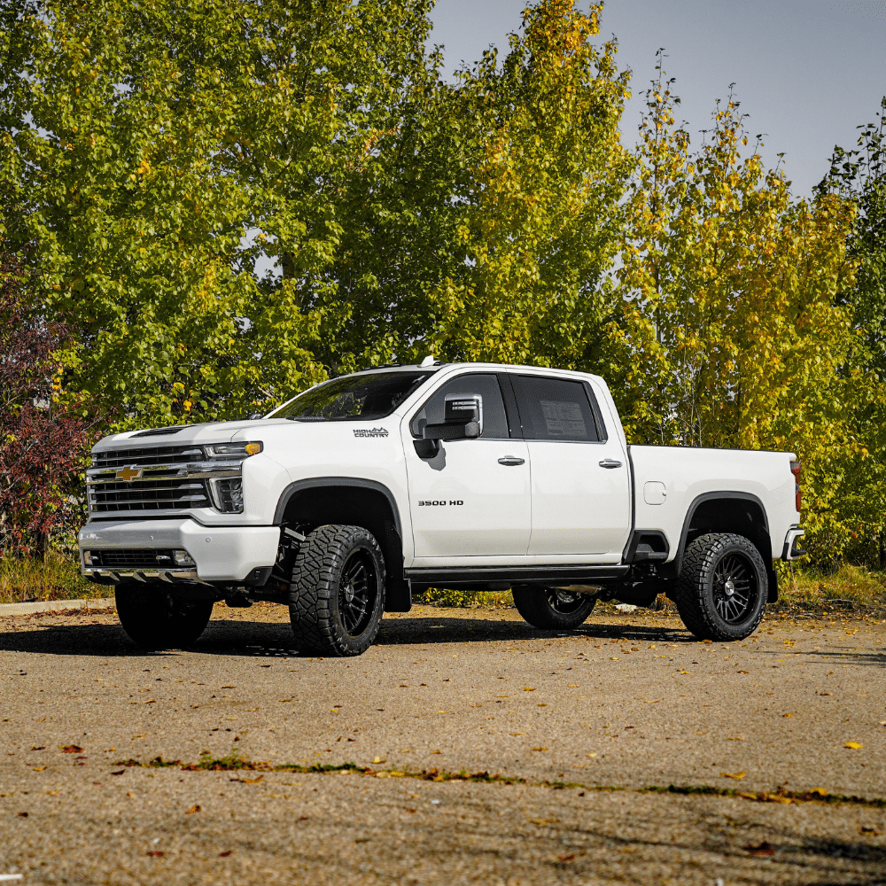 White Chevrolet Silverado 3500 HD truck parked on asphalt, surrounded by green trees.