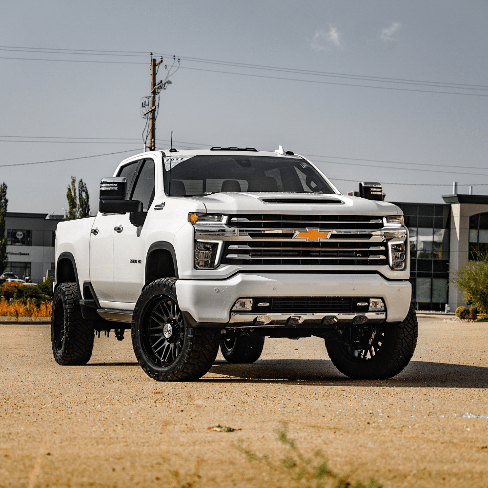 White Chevrolet pickup truck with rugged tires parked on sandy terrain.