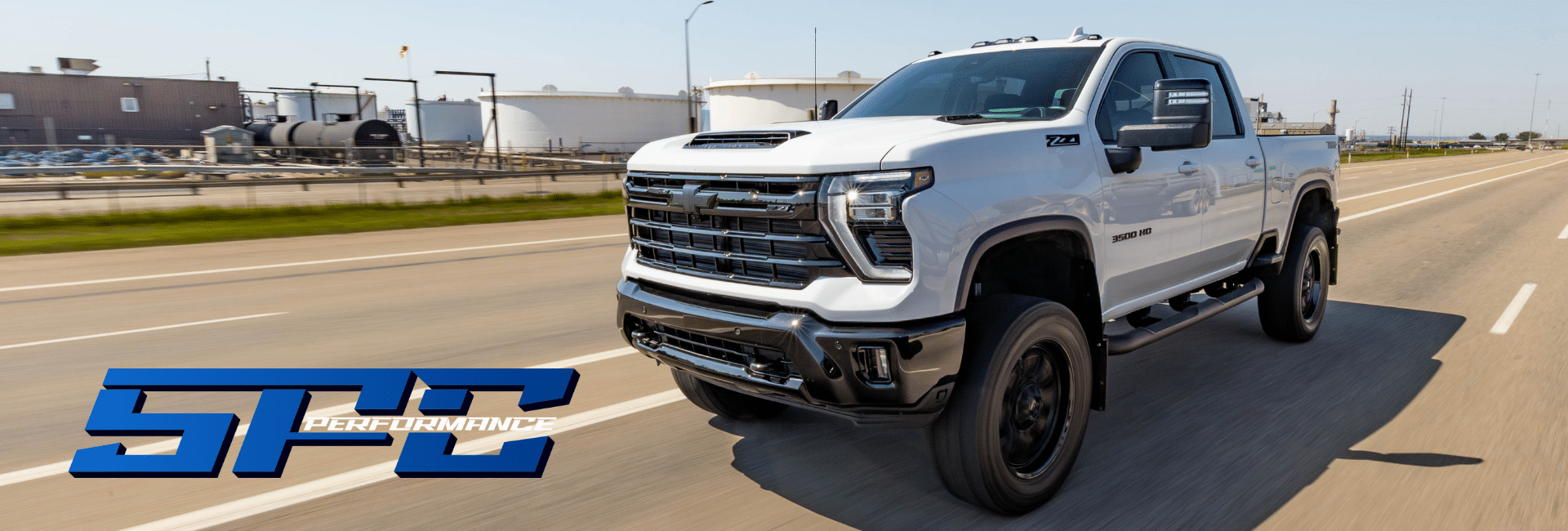 White 3500 HD pickup truck on highway with SPC Performance logo, industrial backdrop.