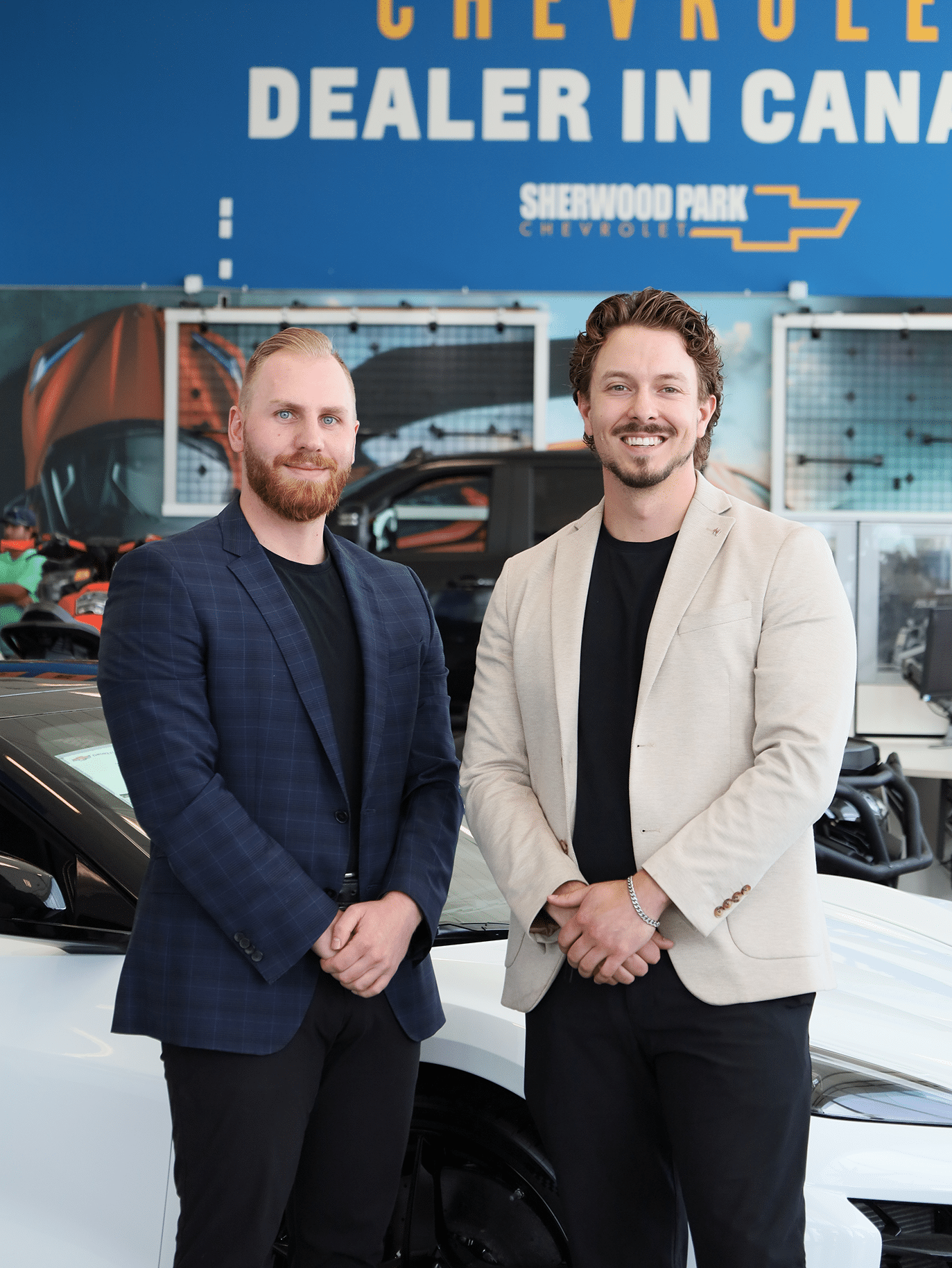 Two men in business attire stand by a white car at a Chevrolet dealership.